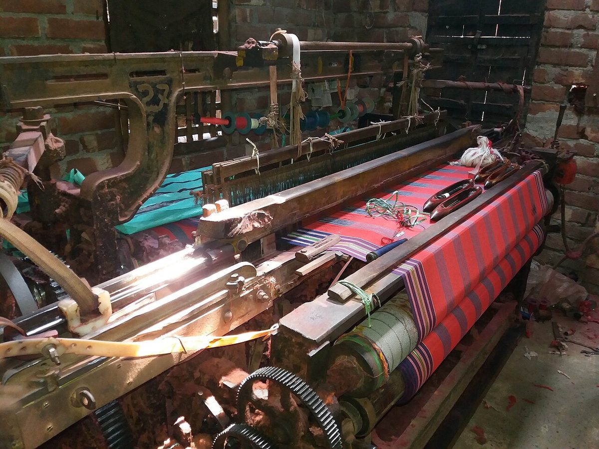 A power loom weaving cloth in a mill shed
